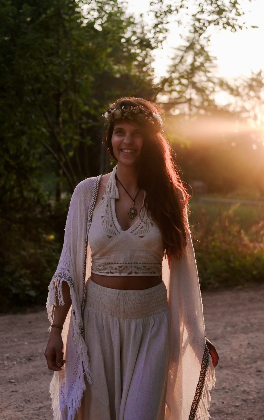 Helena mit Blütenkranz im Haar, in einem hell bestickten Oberteil und weiter Hose, lächelnd im Gegenlicht der Abendsonne